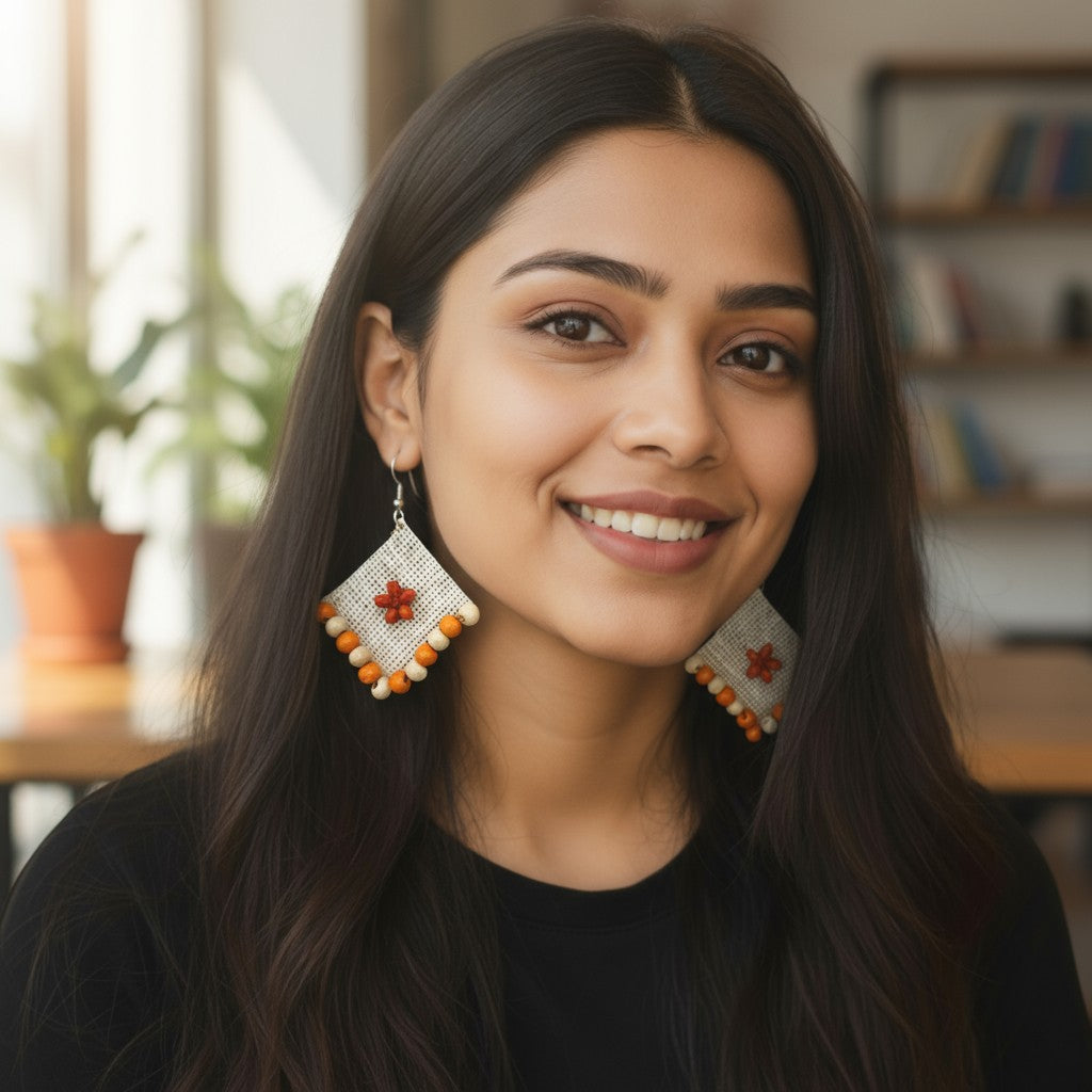 Woman wearing decorative earrings in a casual indoor setting Phool-e-Nazakat white fabric earrings with orange floral appliqué and orange beaded border – Grace of Awadh