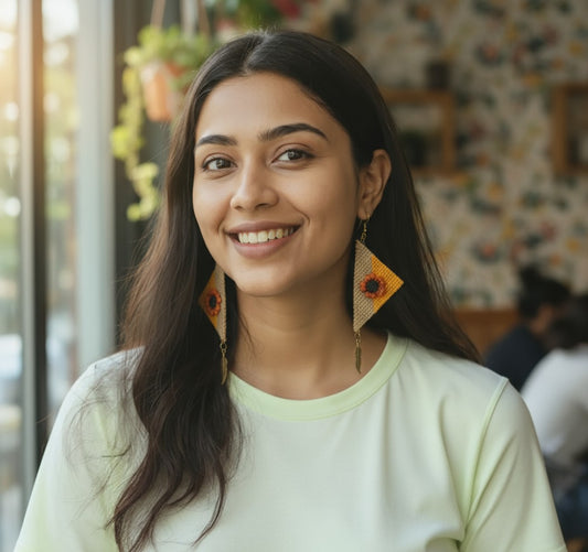 Woman wearing large, colorful earrings in a casual setting Suraj-e-Nazakat handcrafted orange and yellow fabric earrings with floral design and feather charms – Grace of Awadh